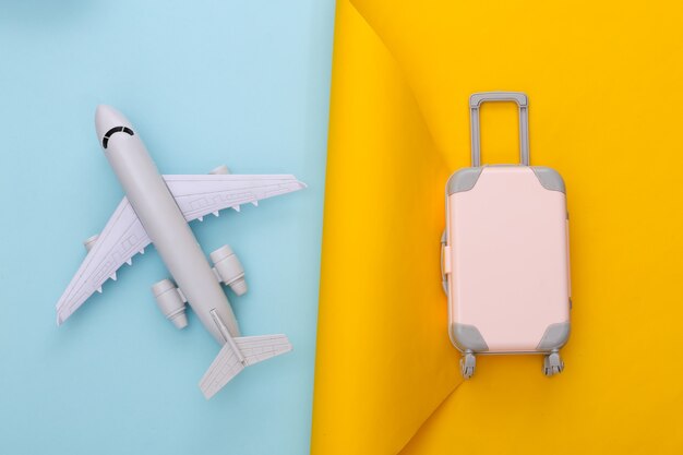 Planificación de viajes. Equipaje de viaje de juguete y avión en azul amarillo. Endecha plana