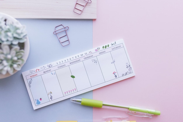 Foto planificador semanal em fundo rosa e azul com canetas e clips
