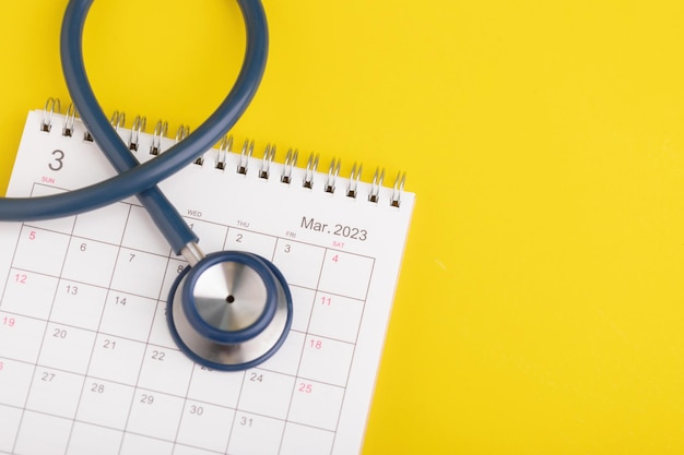 Plankonzept für die Gesundheitskontrolle Die Idee der Zeit für das Gesundheitswesen Nahaufnahme Stethoskop und Tischkalender 2023 auf Gelb Jährliche Planung für das Konzept der Gesundheitskontrolle