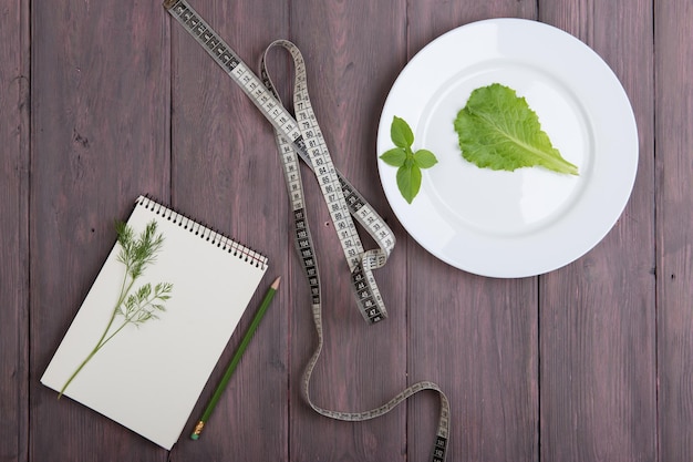 Plankonzept für gesunde Ernährung leerer Notizblock für Rezept Maßband weiße Platte mit Dillsalat Salat Basilikum