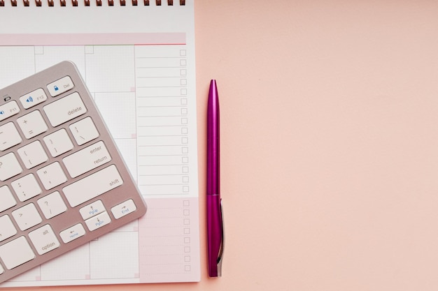 Planner lápis e teclado no plano de fundo rosa para reunião de negócios ou planejamento de viagens