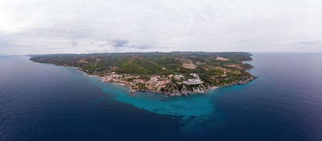 Plano amplio de la costa del mar Egeo de Grecia, edificios de Loutra ubicados cerca de los acantilados rocosos, vegetación y agua azul. Vista desde el dron