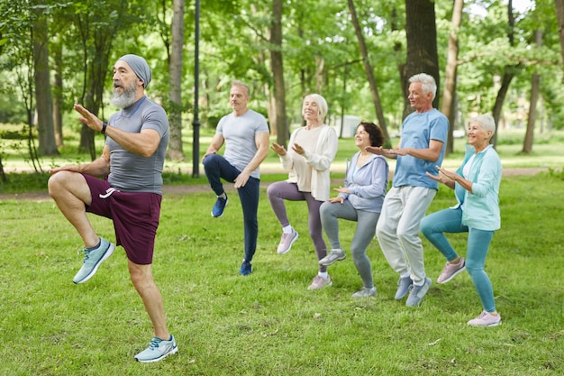 Plano amplio de hombres y mujeres ancianos activos haciendo ejercicio matutino en el parque con entrenador senior
