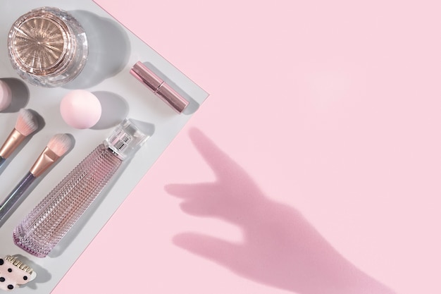 Plano de belleza con accesorios de maquillaje de moda cosmética sobre fondo rosa y gris con sombra de mano. Vista superior, endecha plana, espacio de copia