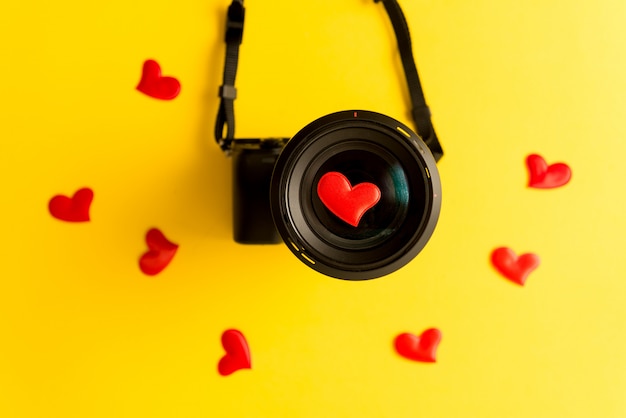 Plano de cámara sin espejo con lente y corazones rojos de amor sobre fondo amarillo