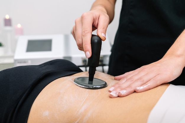 Plano curto de esteticista dando tratamento de radiofrequência a uma mulher no estômago que delineia e estimula a função celular saudável