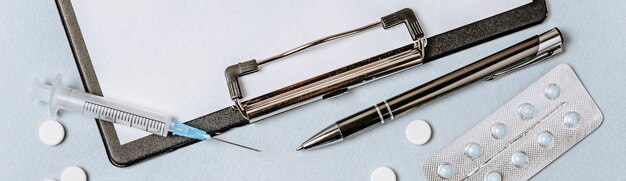 Plano de conceito médico com estetoscópio, pílulas, bloco de notas e caneta na área de trabalho do médico