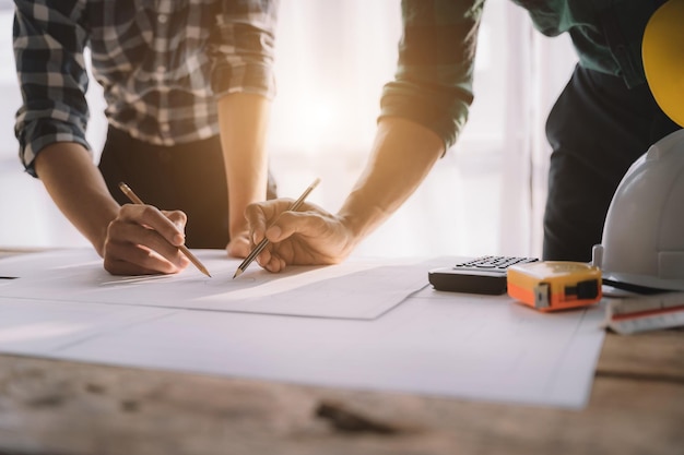 Plano de desenho de mão de engenheiro da pessoa em impressão azul com equipamento de arquiteto Arquitetos discutindo no trabalho em equipe de mesa e conceito de construção de fluxo de trabalho