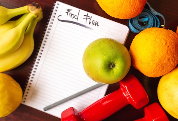 Foto plano de dieta. plano de dieta e frutas e halteres sobre uma superfície de madeira