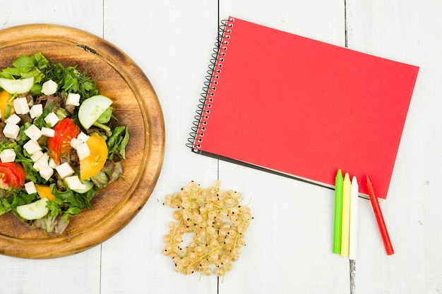 Plano de dieta uma salada de legumes frescos e um caderno em branco sobre uma mesa de madeira branca
