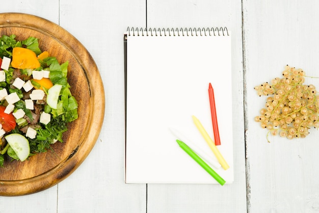 Plano de dieta uma salada de legumes frescos e um caderno em branco sobre uma mesa de madeira branca