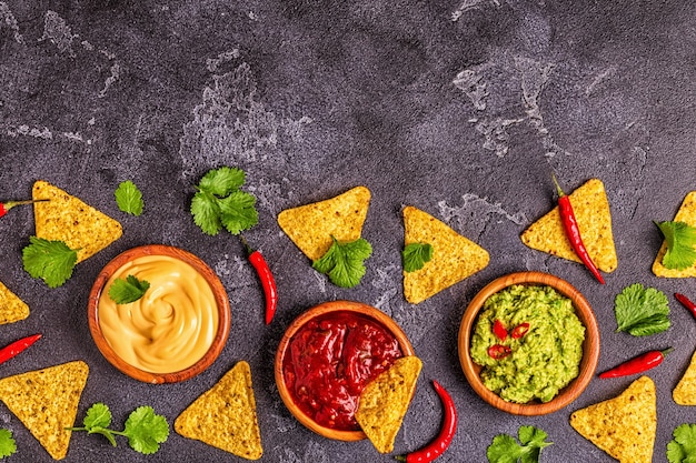 Plano de fundo de comida mexicana: guacamole, salsa, molhos de queijo com ingredientes em fundo preto, vista superior.