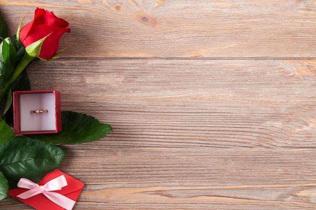 Plano de fundo dia dos namorados com rosa vermelha e anel de ouro na mesa de madeira plana lay cópia espaço