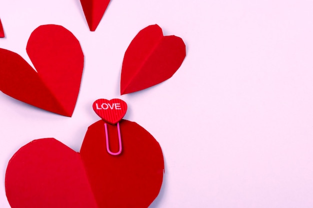 Plano de fundo do dia dos namorados Closeup de corações vermelhos em fundo rosa Clipe de papel com forma de coração e a palavra quotlovequot escrita nele