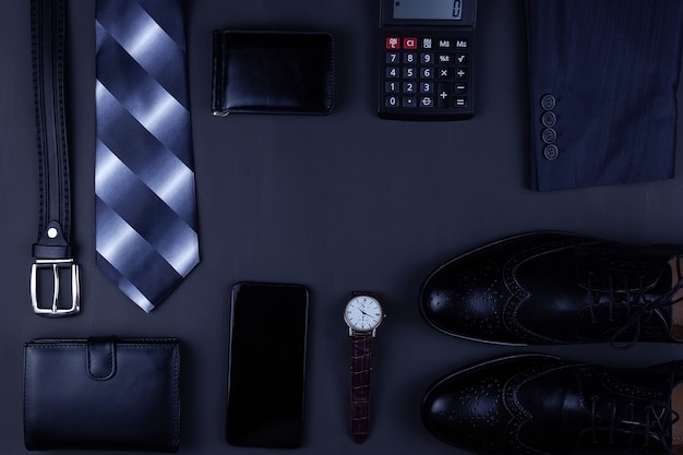 Plano de negócios plano de fundo com um espaço de cópia. sapatos masculinos, carteira de relógio de pulso, cinto, celular e uma gravata em fundo preto.