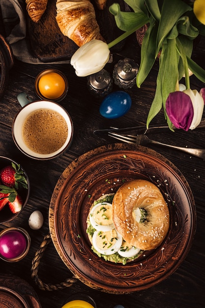 Plano de pequeno-almoço rústico de Páscoa com pães de ovos, tulipas, croissants, ovo, aveia com bagas, ovos de codorna coloridos e decorações de férias de primavera. Vista do topo