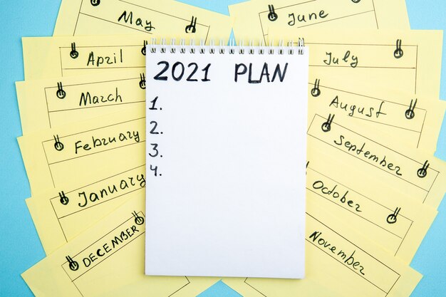 plano de vista superior escrito em cartões de lembrete mensais do caderno espiral na mesa azul