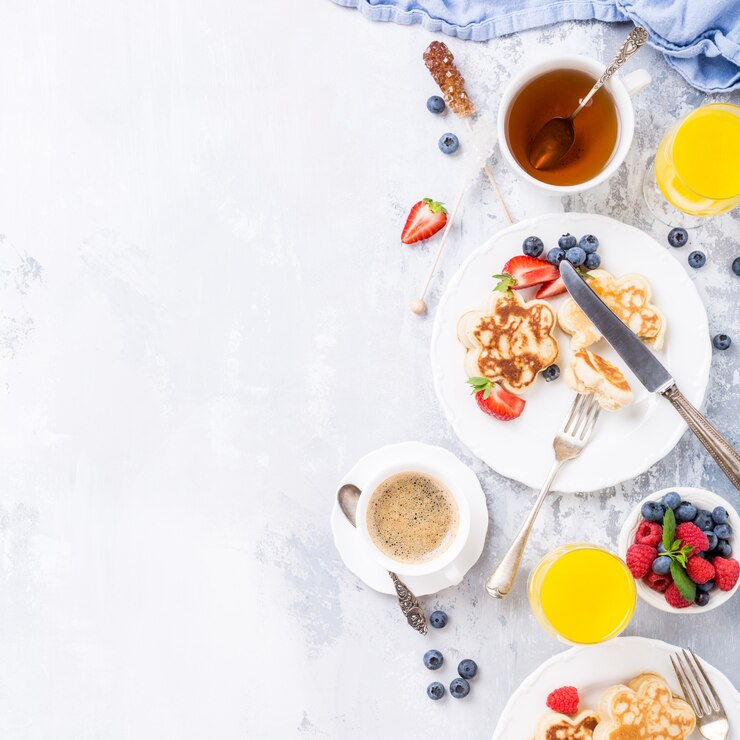Plano con desayuno con panqueques escoceses en forma de flor, bayas y miel en una mesa de madera clara. Concepto de comida sana con espacio de copia.