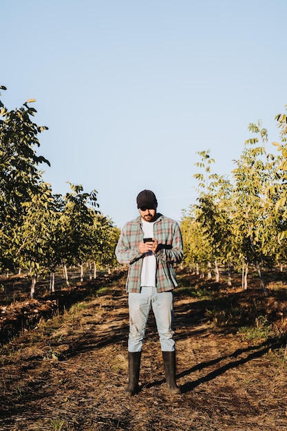 Plano general de un joven agricultor latino usando su teléfono al lado de la plantación de manzanas Concepto agrícola