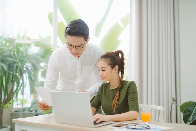 Plano general de una pareja sonriente navegando en una laptop sentada en la mesa