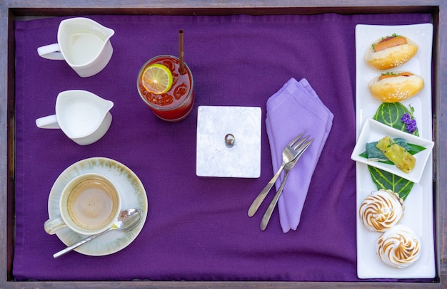 Foto plano de la hora del té con café, té de limón, leche, pan, galletas en un plato blanco con una servilleta morada