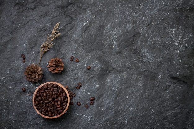 Plano leigos grãos de café em copo de madeira, pinheiros e flores secas em pedra preta