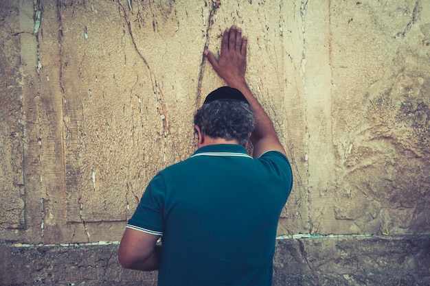 Plano de medio cuerpo de un anciano parado con la mano en alto y tocando el muro de las lamentaciones judío Peregrinación en Jerusalén Israel al muro occidental Persona rezando frente al lugar sagrado judío