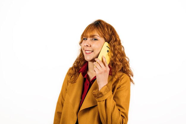 Un plano medio de una mujer sonriente hablando por teléfono con un abrigo amarillo sobre una pared blanca aislada