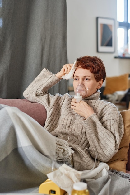 Plano medio vertical de mujer caucásica madura con cabello rojo corto que tiene coronavirus relajándose en ho