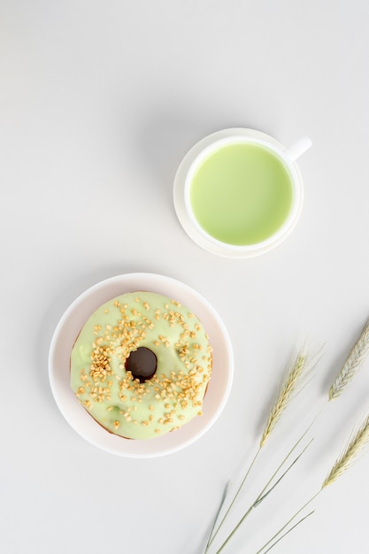 Plano minimalista con taza de té matcha verde, rosquilla de pistacho y tres ruedas de centeno