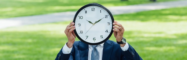 Plano panorámico del hombre de negocios que cubre la cara con el reloj mientras está de pie en el parque
