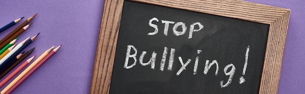 Plano panorámico de pizarra en marco de madera con letras de stop bullying cerca de lápices de colores en