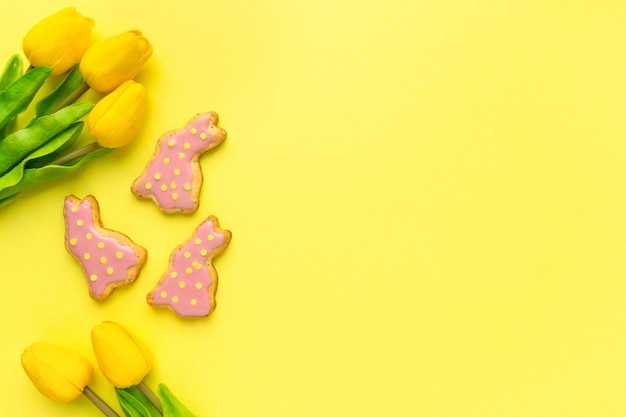 Plano de Pascua Galletas caseras en forma de conejitos con tulipanes sobre fondo amarillo espacio para texto