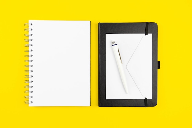 Plano de trabajo de oficina moderno plano con maqueta de cuaderno de papel espiral en blanco, sobre en blanco y bolígrafo sobre superficie amarilla