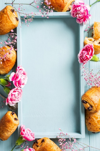 Plano de vacaciones sentar con mini bollos de croissants frescos con chocolate y flores de clavel sobre una superficie azul turquesa. Vista superior. Copia espacio