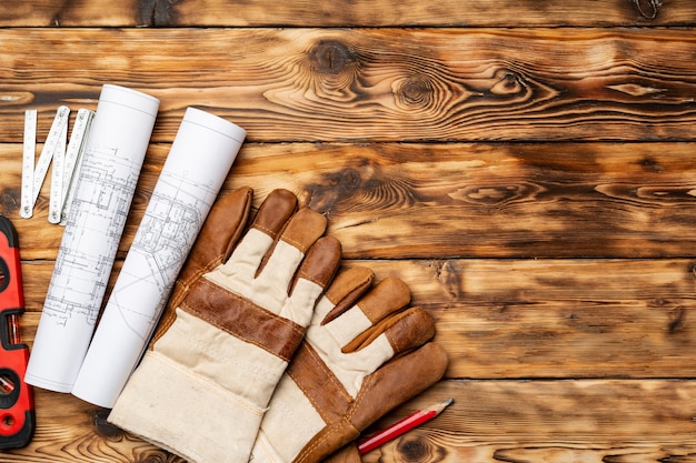 Planos, nivel y guantes de un trabajador de la construcción en la mesa de madera