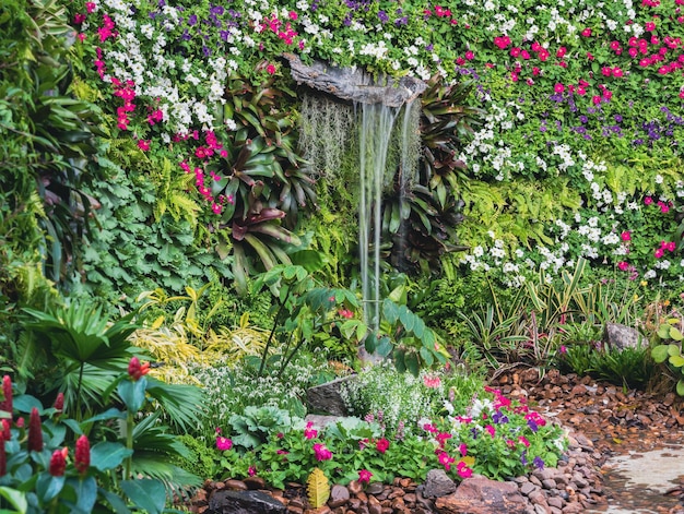 Planta de hojas verdes exuberantes y pared decorativa de jardín de flores con cascada