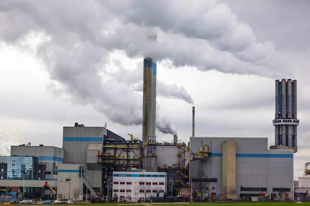 Planta industrial com chaminés de onde sai fumaça espessa para um céu nublado