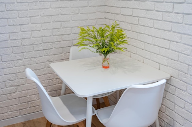 Planta verde en jarrón sobre mesa con pared de ladrillo blanco