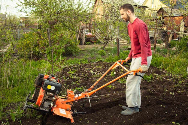 Plantar verduras bajo el tractor de empuje Un hombre con un tractor de empuje en el jardín Trabajo manual con equipo Un anciano le enseña a un niño a arar la tierra