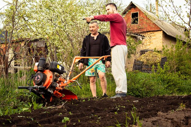 Plantar verduras bajo el tractor de empuje Un hombre con un tractor de empuje en el jardín Trabajo manual con equipo Un anciano le enseña a un niño a arar la tierra