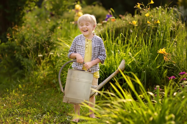 Plantas molhando do menino bonito da criança no jardim no dia ensolarado do verão.