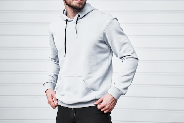 Una plantilla de maqueta de una sudadera blanca con capucha usada por un hombre Un concepto de diseño para la impresión y la marca Un joven posa al aire libre en un estilo casual y de moda de la calle No se muestra la cara