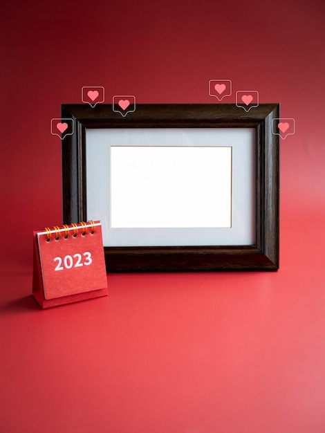 Plantilla para marco de fotos para tarjeta y pequeño calendario de escritorio rojo de 2023 años y amor como iconos de corazón sobre fondo rojo minimalista Espacio en blanco vacío en marco de madera vintage vertical