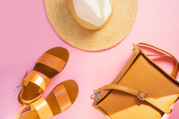 Foto plantilla con sandalias de cuero marrón, sombrero de paja y bolso de color arena sobre fondo rosa. accesorios femeninos concepto de vacaciones de viaje de verano. kit de venta. copia espacio