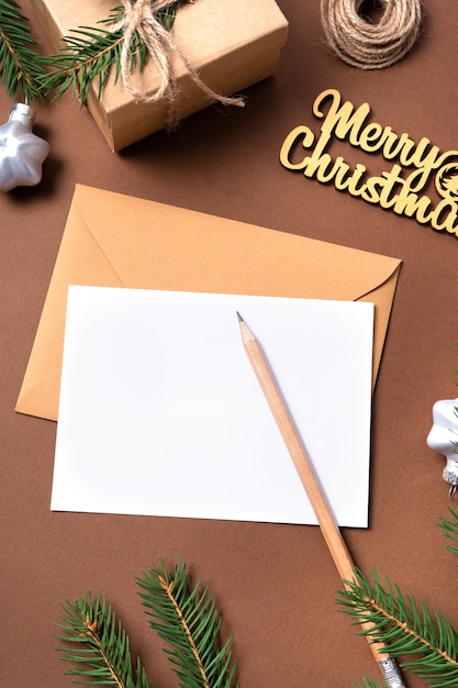 Plantilla de tarjeta de Navidad blanca en blanco sobre fondo beige. Ramas de abeto, adornos navideños, lápiz, lfat lay. Navidad ecológica