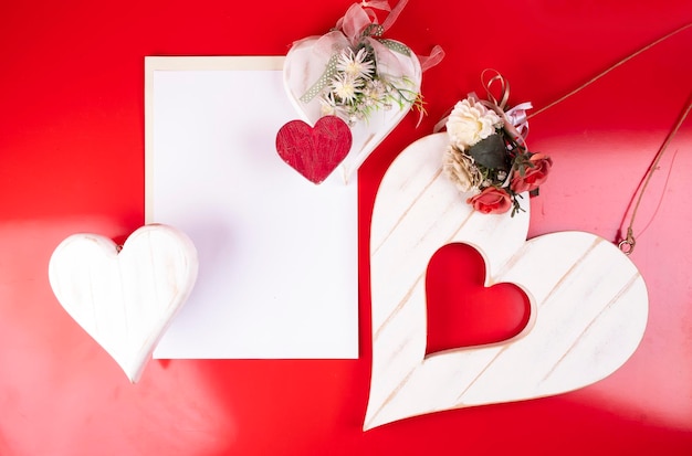 Plantilla de tarjeta de San Valentín con hoja de papel en blanco y corazones de madera pintados a mano con arreglo floral artesanal sobre fondo rojo