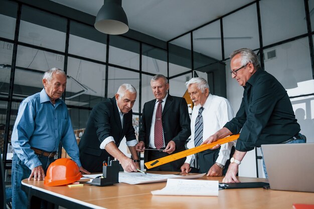 Planung des Baus durch Vermessen auf Papier. Ein gealtertes Team älterer Geschäftsmannarchitekten trifft sich im Büro.