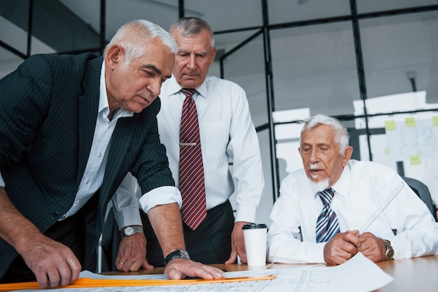 Planung des Baus durch Vermessen auf Papier. Ein gealtertes Team älterer Geschäftsmannarchitekten trifft sich im Büro.