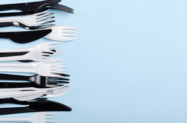 Plástico blanco y negro desechables tenedores y cuchillos sobre un fondo azul. Platos de plastico. Copia espacio, vista superior, endecha plana.
